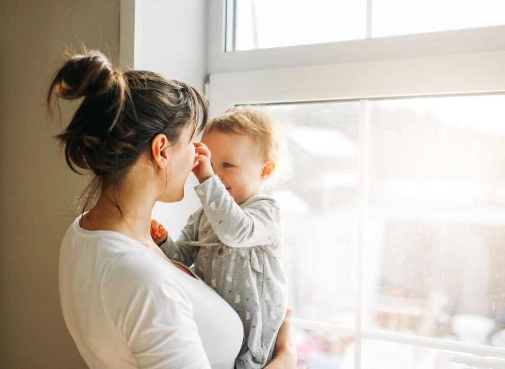 Adorable toddler with mother by sunny window, promoting savings for young children.