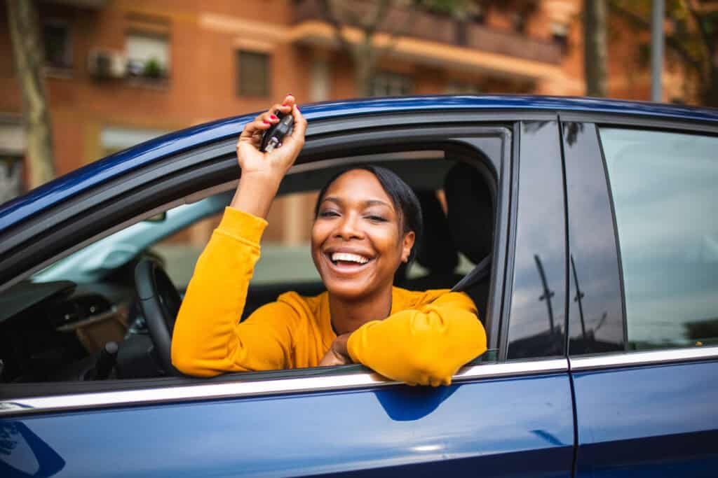Woman smiling and handing over car keys from a blue vehicle.