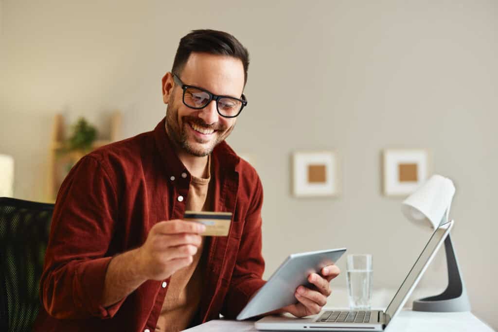 Man holding a VISA prepaid card at his desk with a laptop.